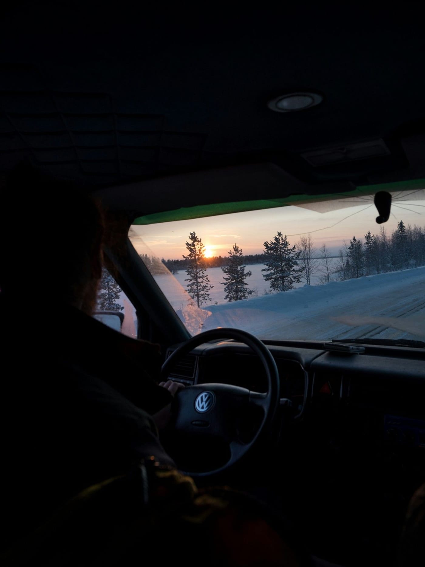 Sürücü koltuğundan karlı bir kış yolu ve gün batımı